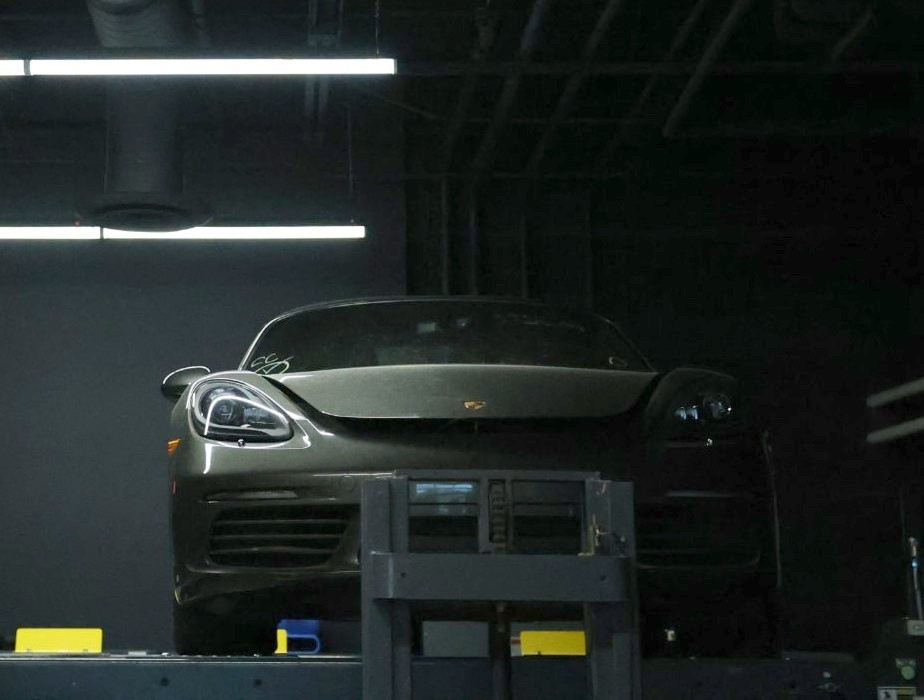 Dark sports car raised on a service lift in a garage lit by overhead linear LED fixtures wired by iPowerDenver